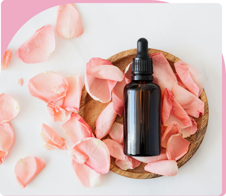 A bottle of essential oil sitting on top of pink petals.