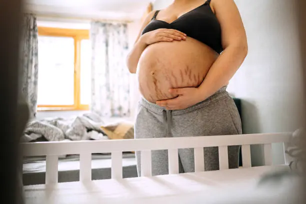 A pregnant woman standing in front of a crib.